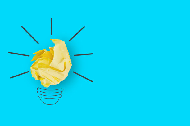 一张皱巴巴的黄纸和一张图片放在办公室的蓝色桌子上，做成了一个灯泡。前视图。灵感的概念。为你的文本复制空间图片下载