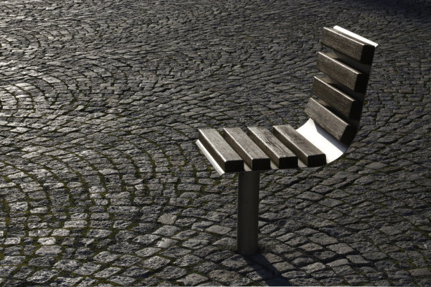 个人的长椅上。安装在城市广场上的一把椅子。现代城市环境中隐私和隐居的可能性。背光户外照片的不寻常的长凳，以路面的石头/鹅卵石为背景。图片下载
