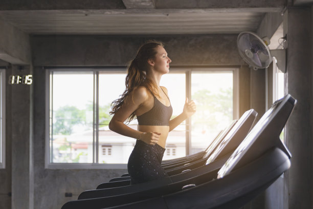 封闭式快乐年轻女子在现代健身房跑步机上锻炼，健康的生活方式理念。图片下载