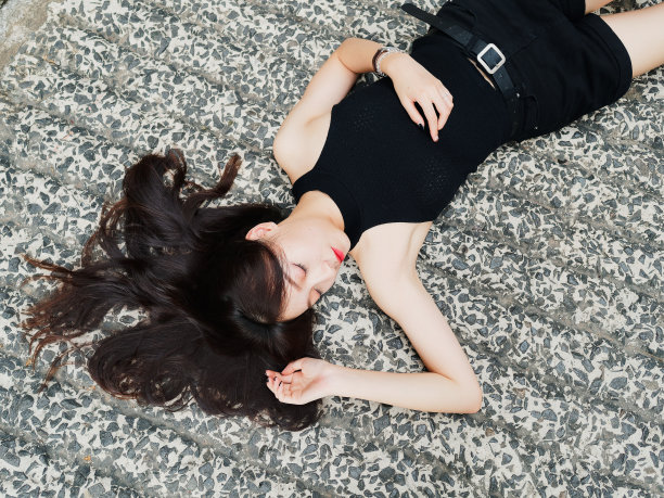 高角度的一个漂亮的女人有黑色的长发在黑色的连衣裙上闭着眼睛躺在地上，浪漫的年轻女性有一个美好的梦想肖像。图片下载