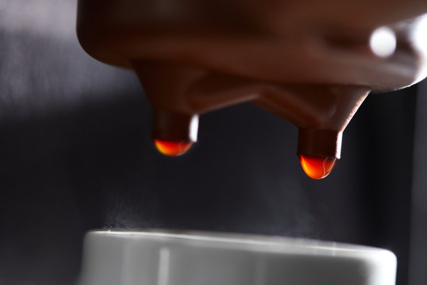 在咖啡机滴咖啡到一个杯子的微距照片。制作饮料的过程图片下载