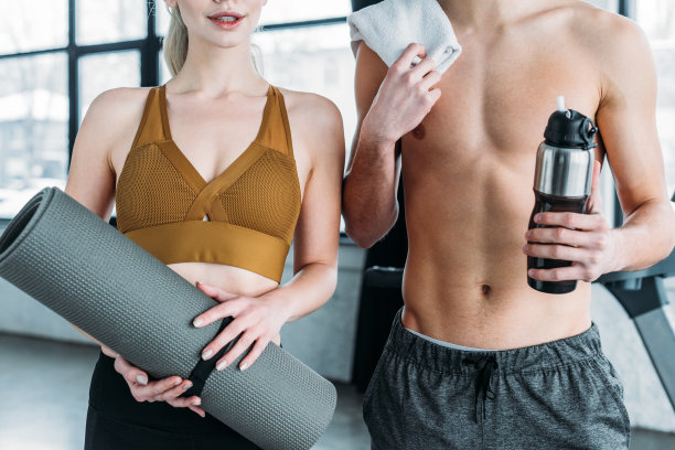剪短的照片的女人与瑜伽垫和赤膊男子与毛巾和运动瓶站在一起在健身房图片下载