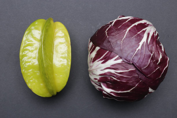 杨桃和意大利菊苣。几杯甜的和苦的。东部和西部。深蓝色背景上的天然纯素或素食食品的概念样本。传统的欧洲莴苣/卷心菜和异国水果。图片下载