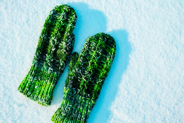 阳光明媚的冬日，雪背景面。一双绿色羊毛针织连指手套，暖场概念。图片下载