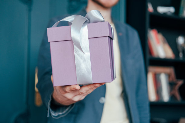 礼盒与灰色银色丝带在手中的年轻迷人的男子在蓝色背景图片下载
