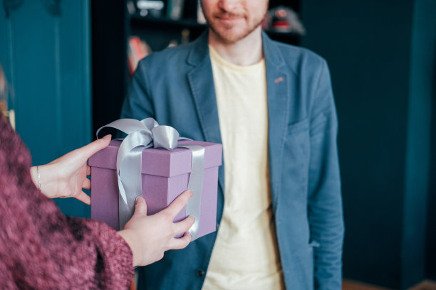 女人得到礼盒与灰色银色丝带从年轻迷人的男子在蓝色背景图片下载