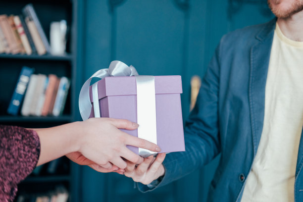 女人得到礼盒与灰色银色丝带从年轻迷人的男子在蓝色背景图片下载
