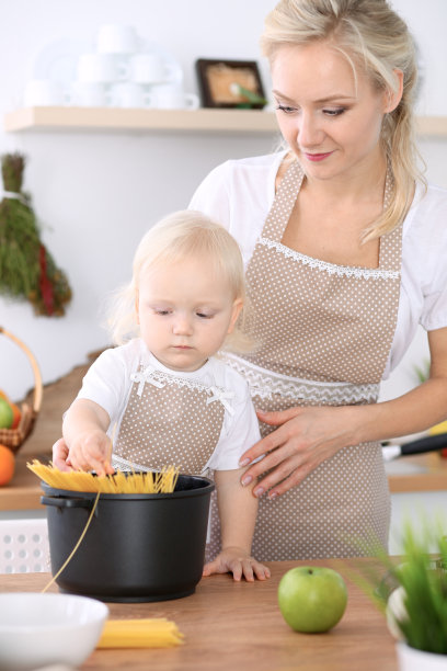 快乐的妈妈和小女儿在厨房做饭。花时间在一起，家庭乐趣的概念。图片下载