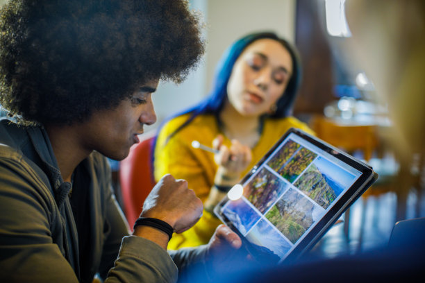 美国黑人用平板电脑找照片。一群多民族的人在餐厅休息室开会。团队合作、企业、多样性和社会观念。图片下载