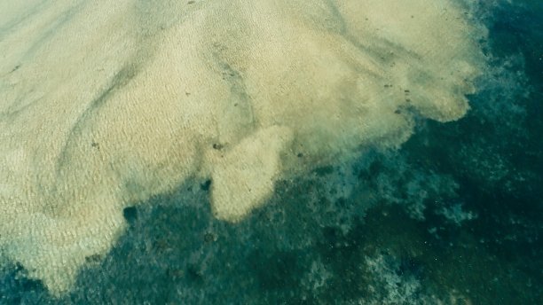 无人机拍摄的这张令人惊叹的照片:在一个偏远的热带小岛周围，一个巨大的珊瑚礁与一个风平浪静的沙滩相遇，水面平坦，令人难以置信的彩色海床图片下载