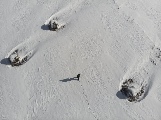 成年男子徒步旅行者在被雪覆盖的田野徒步旅行。鸟瞰图，正上方。图片下载