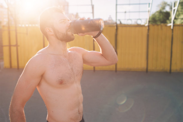一个年轻的运动员训练后的照片。英俊的年轻肌肉男喝蛋白质。迷人的运动赤膊运动员饮用运动营养奶昔从搅拌机。图片下载