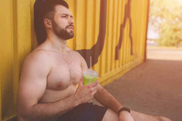 英俊的年轻肌肉男喝绿色排毒奶昔杯。一个年轻的运动员训练后的照片。图片下载