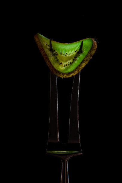 鲜嫩多汁的绿色猕猴桃切片，银叉放在深色背景上。健康食品的概念。关闭了。图片下载