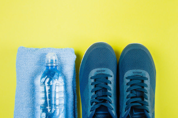 黄色背景上的蓝色运动鞋、毛巾和水瓶。运动设备。健康生活理念。平铺，俯视图，拷贝空间图片下载