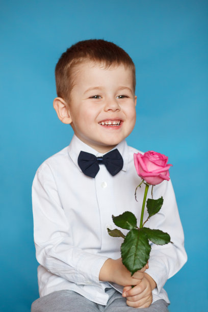 一个英俊的小男孩拿着一朵粉红色的玫瑰图片下载