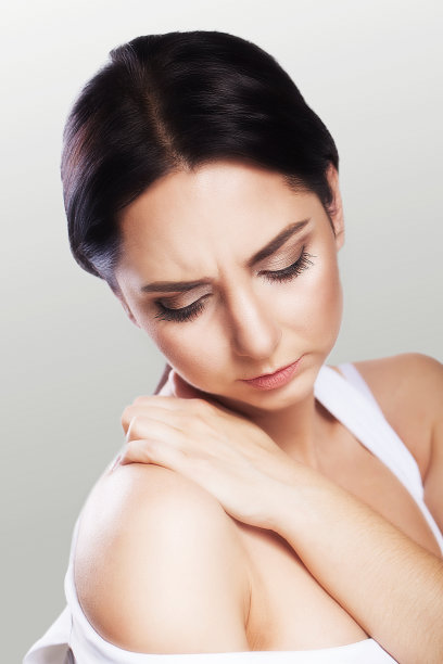 肌肉疼痛。一位年轻女子把手放在肩膀上。冷。过度疲劳。健康的概念。在一个灰色的背景。图片下载