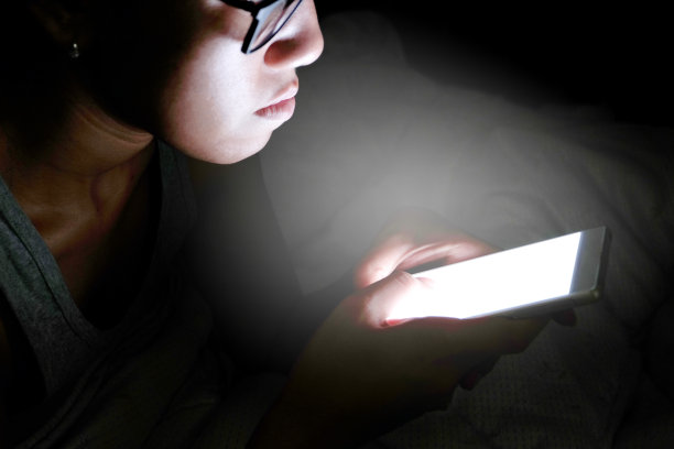 女人不睡觉，晚上压力很大。她在没有光线和黑暗的卧室里使用和查看智能手机。图片下载
