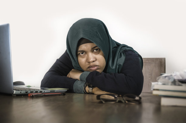 戴着头巾，感到压力巨大、不堪重负的穆斯林女学生正在用笔记本电脑和大学课本复习备考图片下载