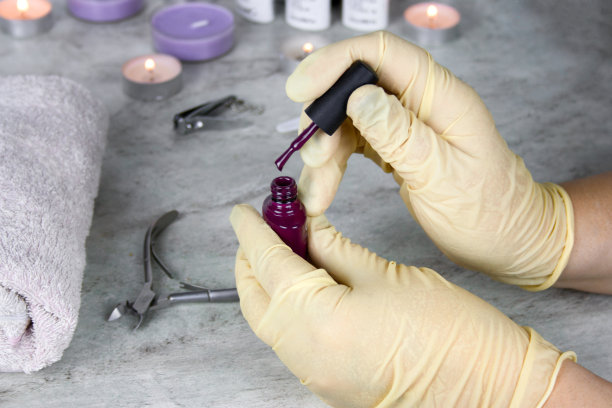 手的美甲师在医疗橡胶手套与一瓶红色指甲油图片下载