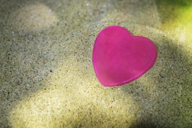 粉红色的心在阳光的沙面上。图片下载
