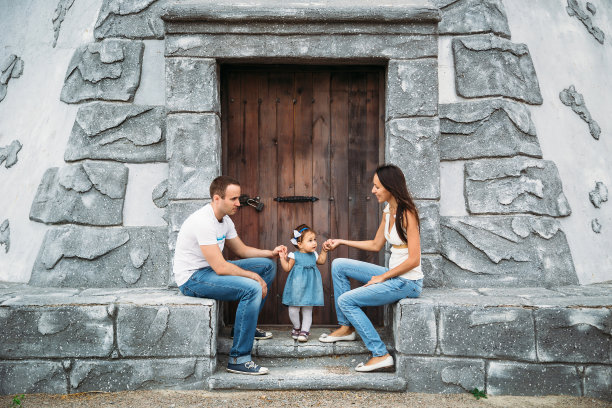 快乐的年轻家庭穿着白色t恤和蓝色牛仔裤和一个穿着裙子的小女儿坐在附近的灯塔和玩耍图片下载