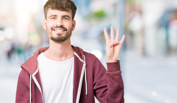 年轻英俊的男子在孤立的背景下展示和指着第四个手指，同时自信和快乐的微笑。图片下载