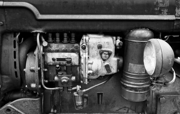 一个大型旧汽油发动机的黑白图像与锈迹和旧污渍在一个深色的农业车辆与前灯图片下载