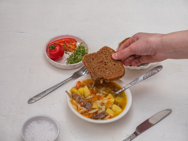 女孩的手拿着一片黑面包放在一盘热汤上。图片下载