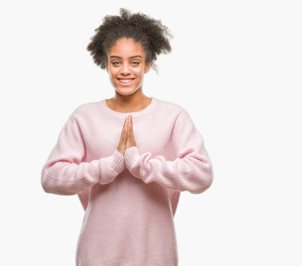 年轻的美国黑人妇女穿着冬季毛衣越过孤立的背景，双手一起祈祷，以自信的微笑请求宽恕。图片下载