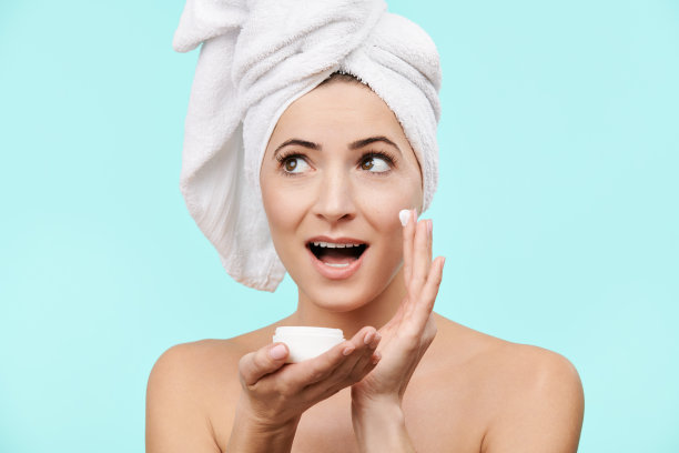 迷人的35岁左右的女人在脸上涂抹保湿霜。迷人的白人妇女的照片与健康的皮肤隔离在柔和的蓝色背景。美容护肤理念。图片下载