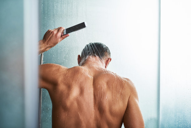 年轻男子在浴室洗澡时使用手持式淋浴喷头图片下载