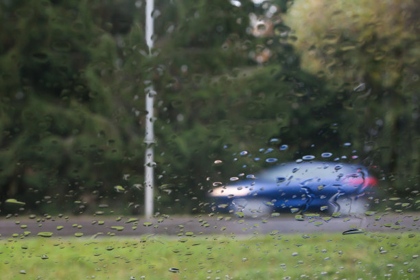 雨滴落在汽车玻璃上，注意雨滴。可以看到街道和正在行驶的汽车。长时间曝光的照片。图片下载