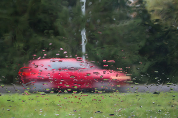 雨滴落在汽车玻璃上，注意雨滴。可以看到街道和正在行驶的汽车。长时间曝光的照片。图片下载