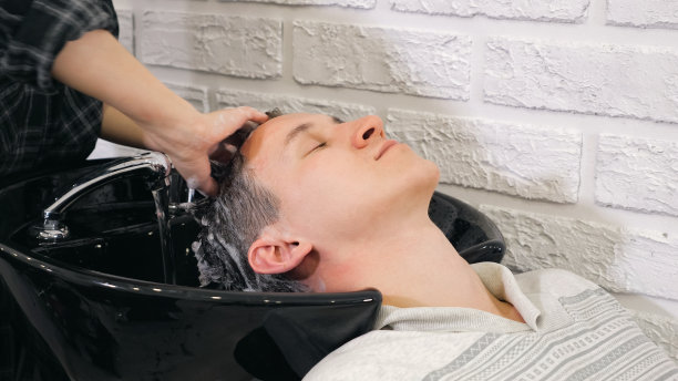 理发师在理发店用流动的水洗深色男性头发。图片下载
