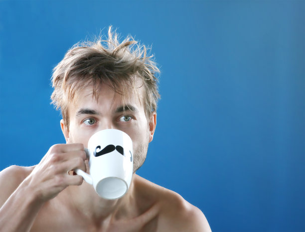 刚醒来，披头散发的男人喝新鲜的咖啡或茶从马克杯与涂黑胡子，工作日早上，蓝色背景图片下载