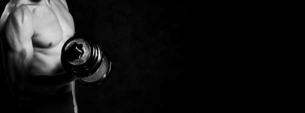 近距离的肌肉男子做运动与哑铃在灰色的背景。黑白照片图片下载