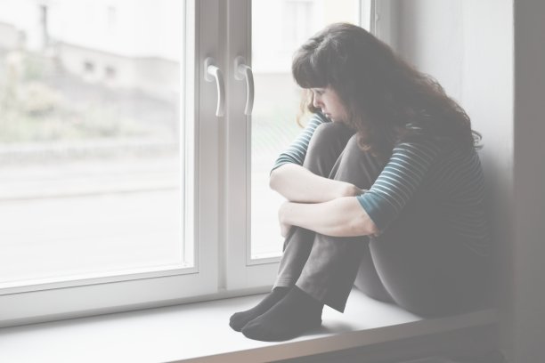 悲伤的年轻女人坐在窗户上，看着窗外图片下载