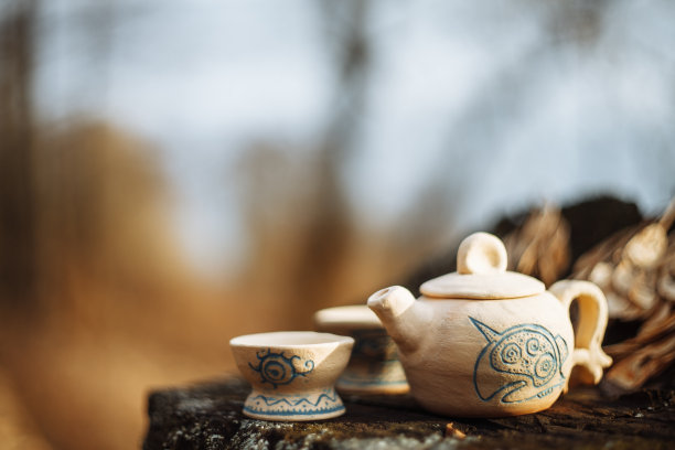 树桩上的泥白色蓝纹茶壶和两个饮用碗。手工。图片下载