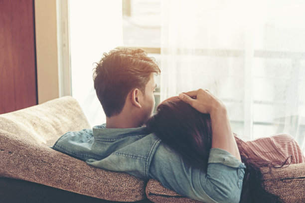 在阳光明媚的日子里，情侣们坐在家里的沙发上放松，透过客厅的窗户眺望窗外。图片下载