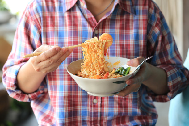 女人手握筷子的方便面杯在餐厅，钠饮食高风险肾衰竭，健康的饮食观念图片下载
