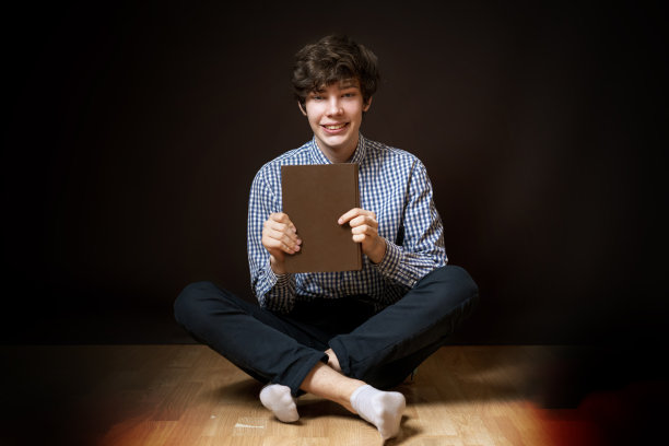 肖像的十几岁的学生坐在地板上读一本书在黑暗的背景孤立的b图片下载