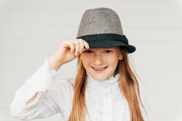 特写的漂亮小女孩的8-9岁的白色木制背景。穿着白色复古衬衫和灰色黑色帽子的孩子图片下载