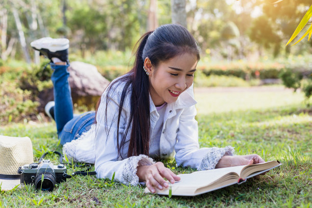 一个年轻的亚洲女人躺在公园里看书图片下载