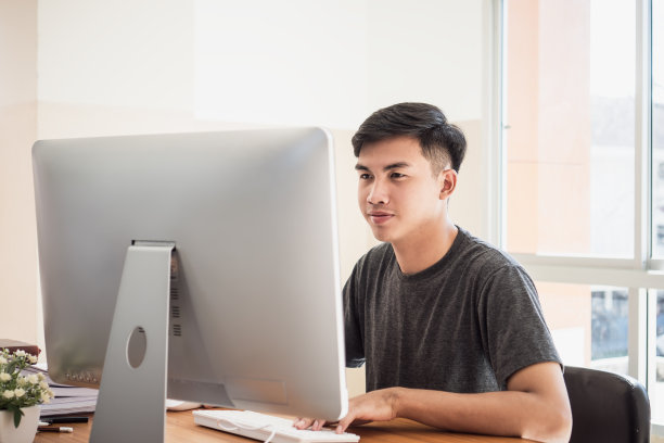 有吸引力的亚洲商人/学生年轻男子坐在办公室技术中心附近的办公桌上的文件报告忙于搜索信息数据互联网图片下载