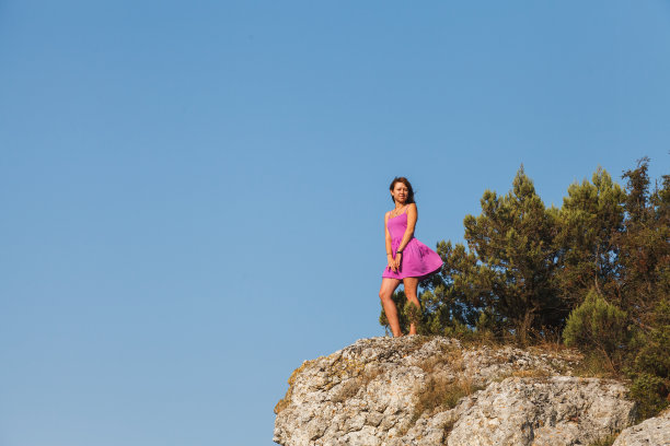 一个穿着粉红色裙子的女孩站在悬崖前的一块岩石上图片下载