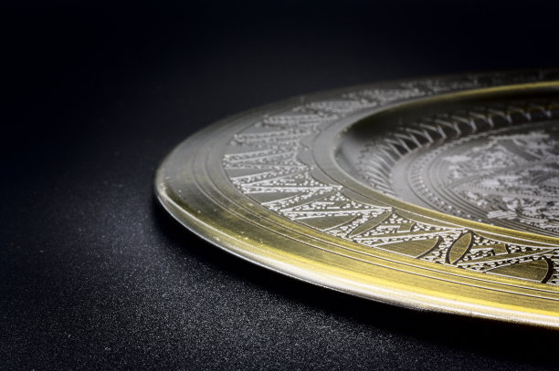 古色古香的金色盘子放在黑色石板桌上，深色的背景与盘子上的轻微阴影图片下载