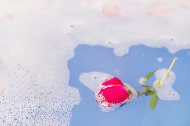 新的陶瓷浴室与泡沫。浴室的健康。蓝色的水和玫瑰花瓣。花瓣芳香疗法。洗个澡。水和白色泡沫。浴室里飘着玫瑰。治疗健康图片下载