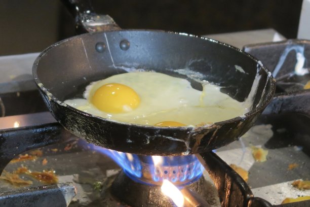 两个煎蛋在小煎蛋卷/煎蛋卷平底锅里煮的图片，酒店餐厅的早餐照片，在肮脏的煤气炉上煎/煮图片下载