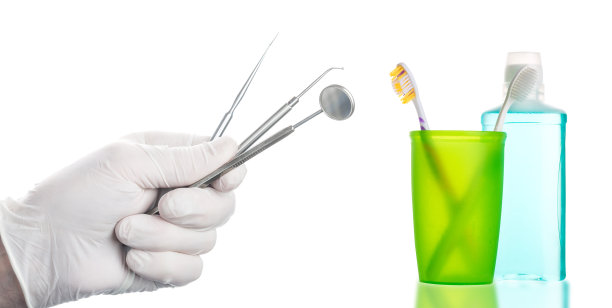 牙科镜和医生的器械放在橡胶手套里，靠近绿色玻璃牙刷和漱口水瓶，白色背景上有自由空间隔离。牙科保健的概念。图片下载